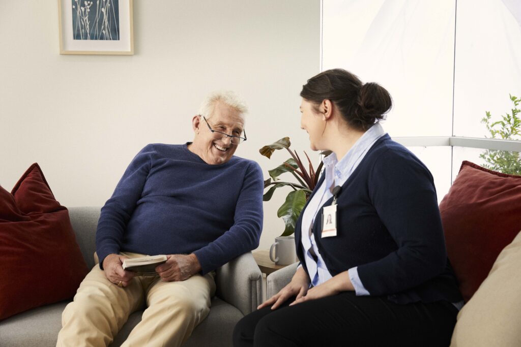 Elderly Male resident laughing with carer sitting on couches